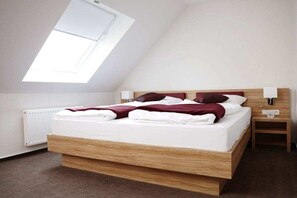 A modern bedroom with a sloped ceiling, a wooden bed frame, a white mattress, and a nightstand with a lamp. - Holiday apartment with 1 bedroom (Lembruch)