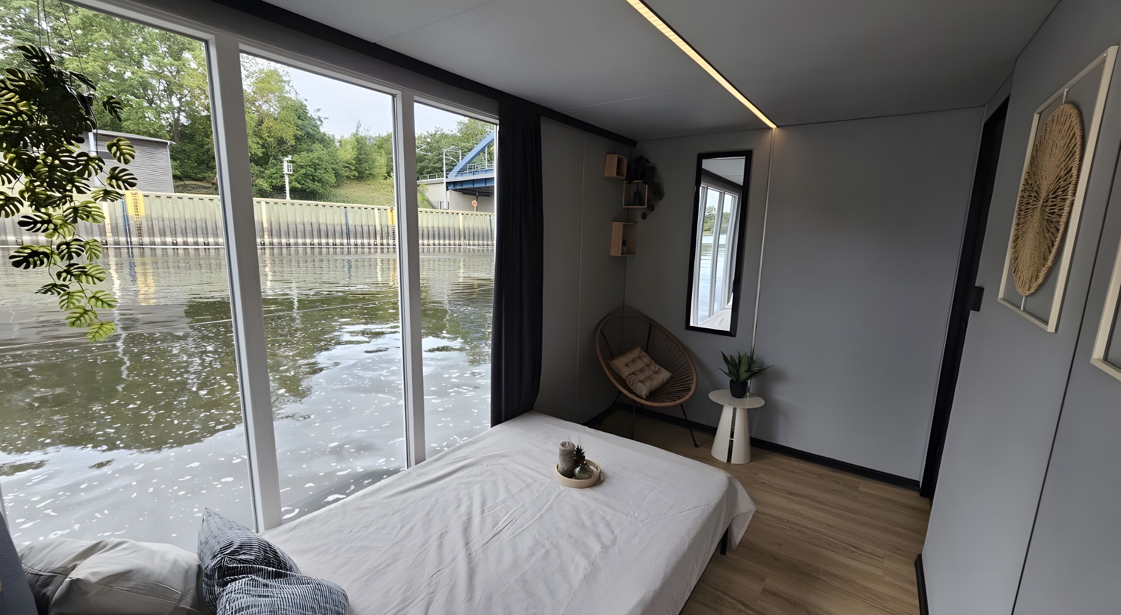 Ett modernt sovrum med ett stort fönster, en säng, en stol och ett litet bord med en växt.