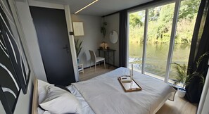 A modern bedroom with a large window, a bed, a desk, and a chair.