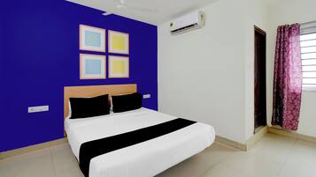 Um quarto com cama, ventilador de teto, ar condicionado, janela com cortinas e quadros nas paredes.