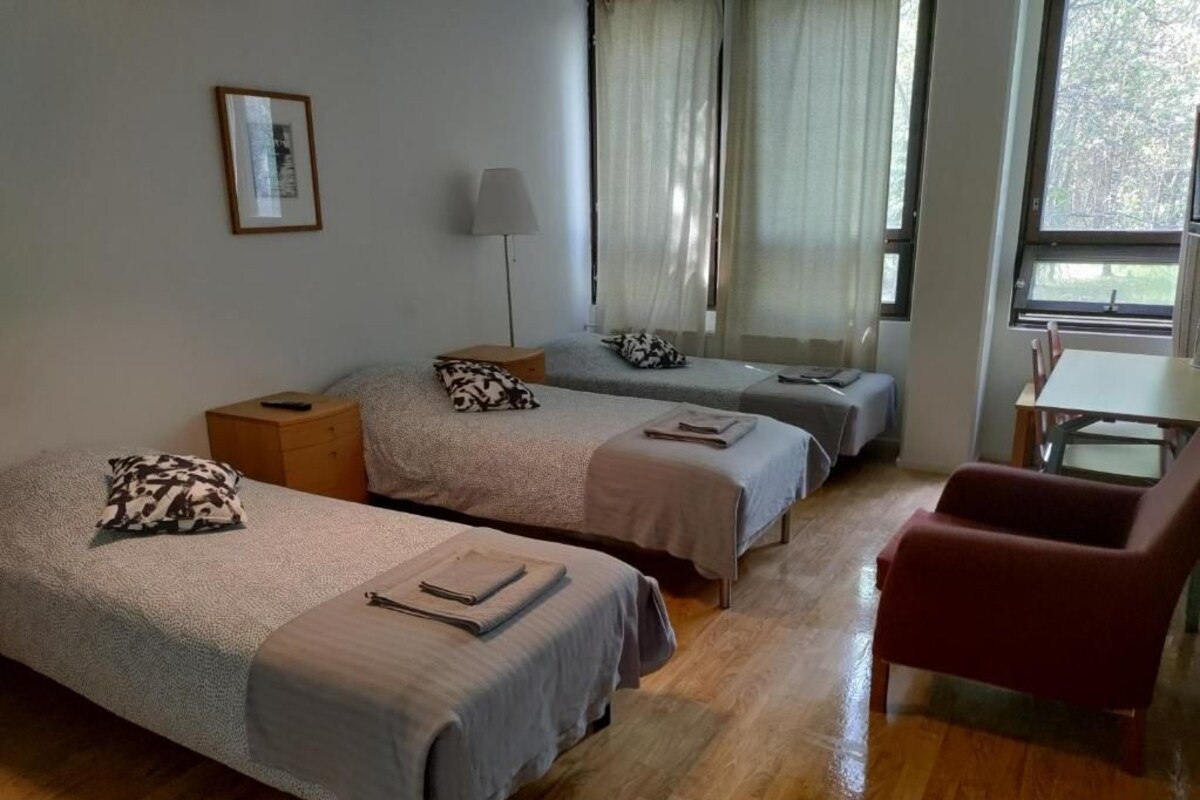Hotellihuone, jossa on kaksi sänkyä, työpöytä, tuoli ja ikkuna, jossa on verhot.