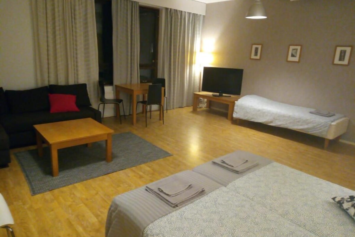 Hotellihuone, jossa on sohva, pieni pöytä, televisio, sänky ja työpöytä.