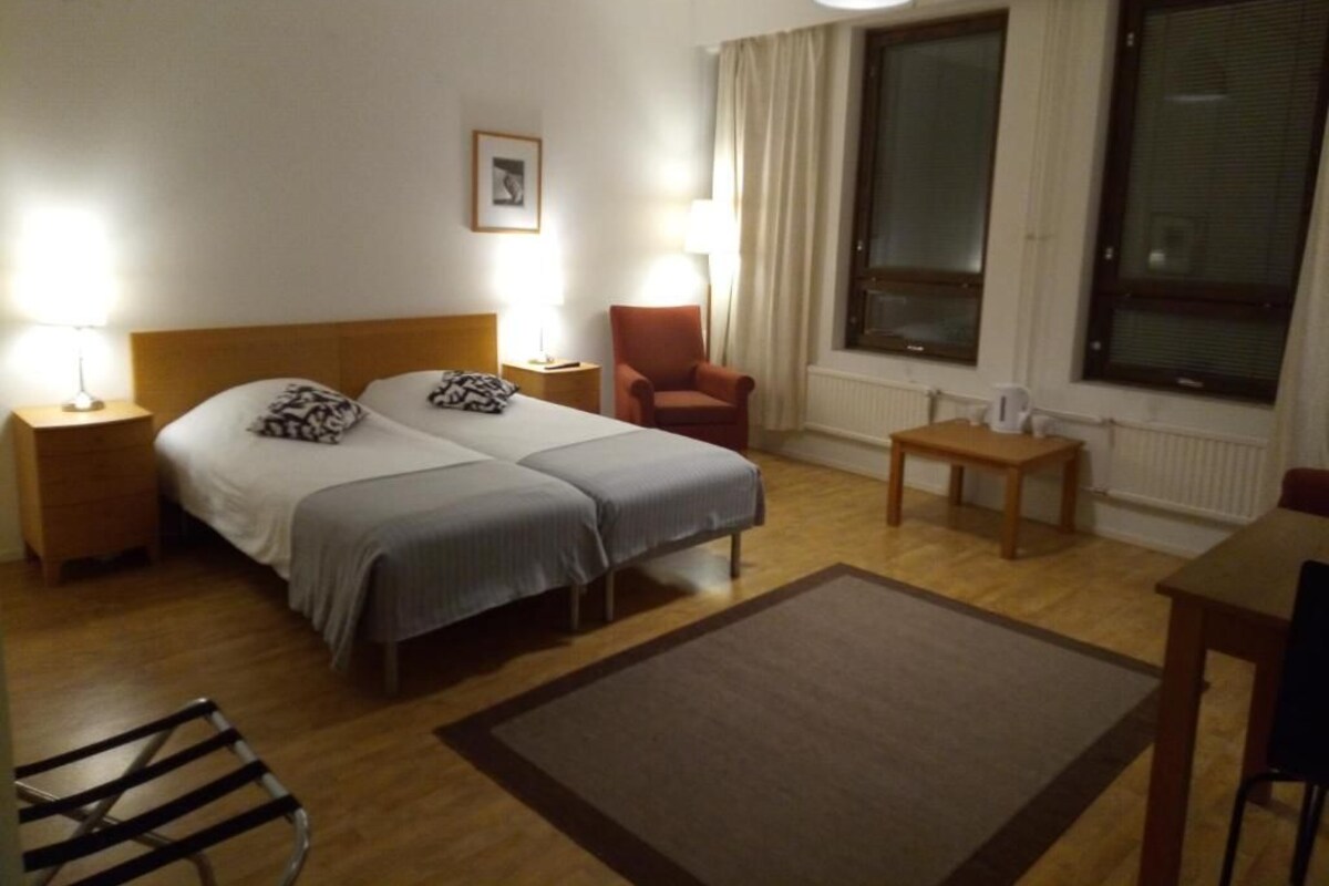 Hotellihuone, jossa on kaksi sänkyä, tuoli, pöytä, lamppu ja ikkuna.
