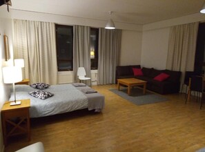 Hotellihuone, jossa on sänky, sohva, pieni pöytä, lamppu ja tuoli.
