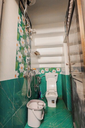 A small bathroom with a toilet, a shower, and a bucket. - The Jawai Niwas (Sumerpur)