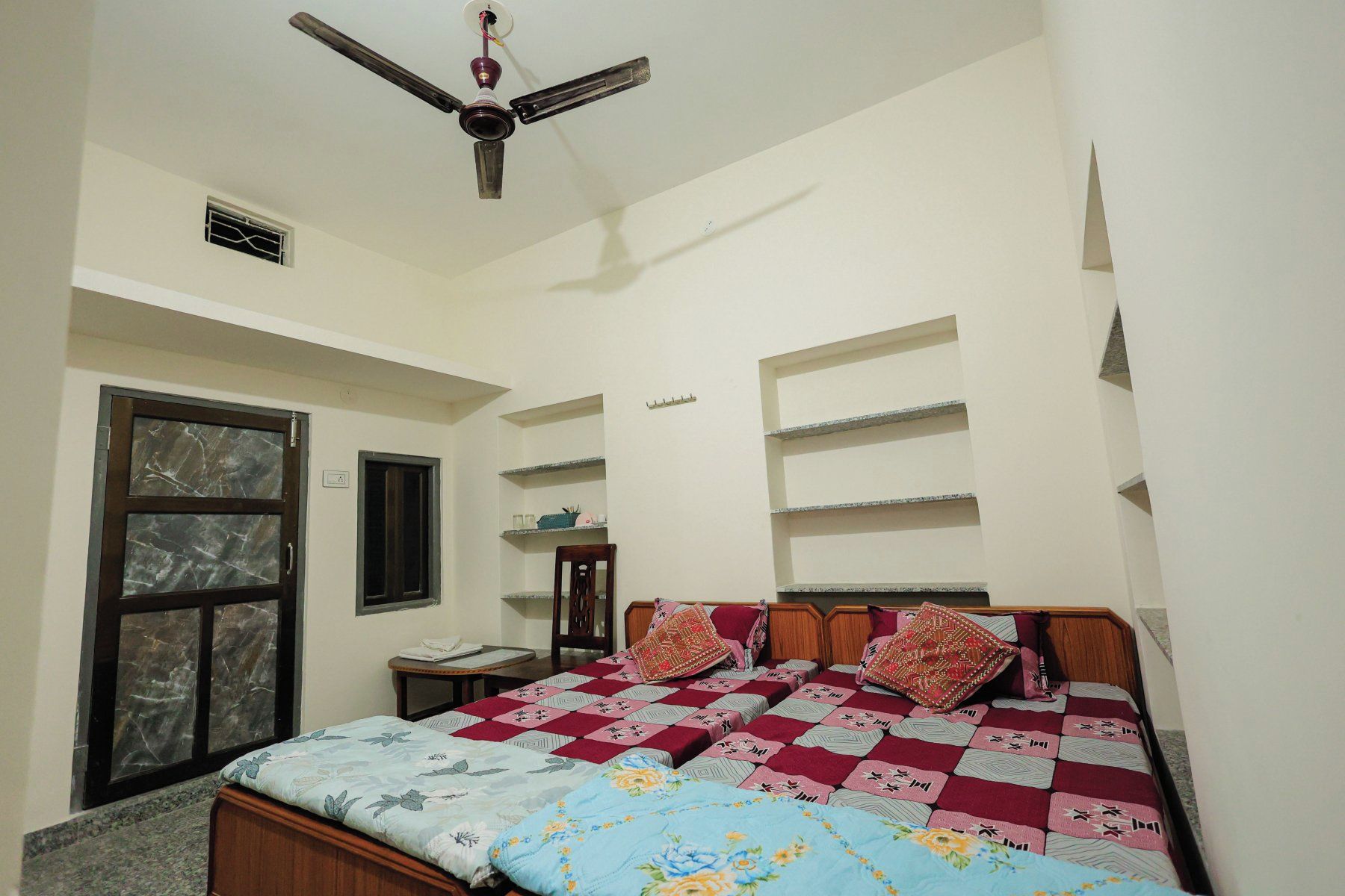 A bedroom with a bed, a ceiling fan, a window, and built-in shelves.