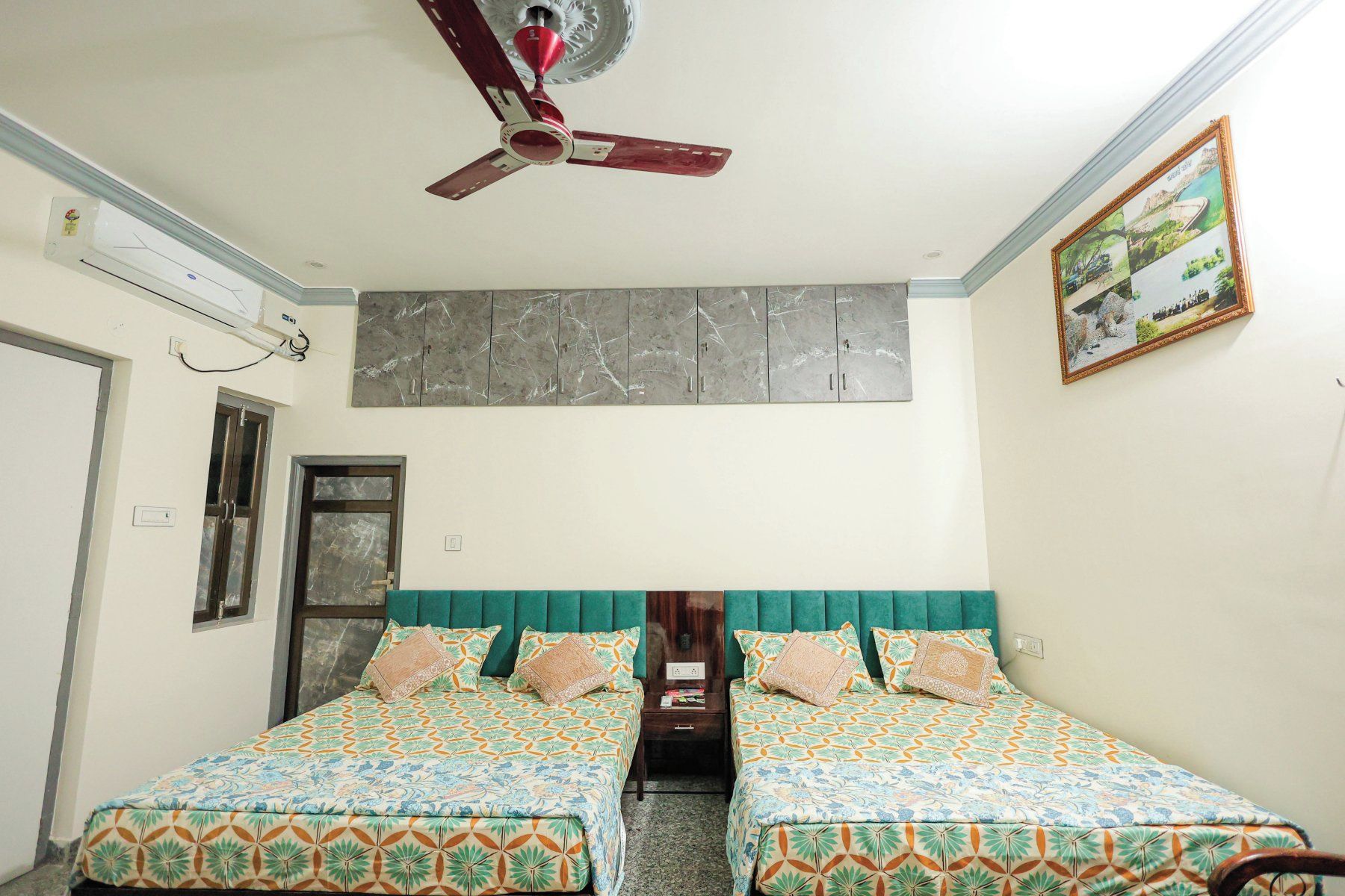 A room with two beds, a ceiling fan, a marble-patterned wall, and a framed photo.
