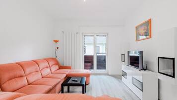 Una sala moderna con sofá, una mesa de centro, televisor y puerta corrediza de vidrio que da a un espacio exterior.