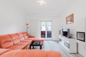 Una sala moderna con sofá, una mesa de centro, televisor y puerta corrediza de vidrio que da a un espacio exterior.