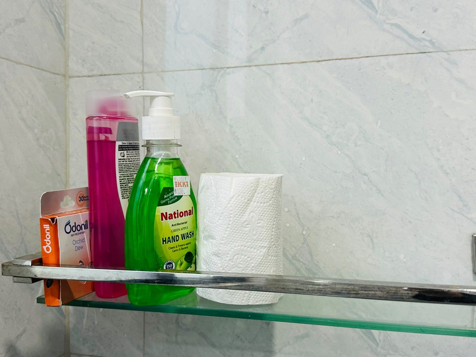 A bathroom shelf with various toiletries including a pink bottle, a green bottle, a white bottle, and a box.