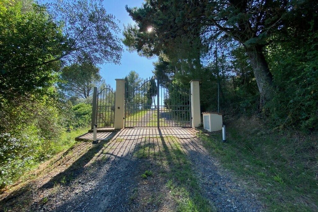 Ein verschlossener Eingang mit einem Metalltor, umgeben von Bäumen und einem Schotterweg.