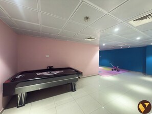 A pool table in a room with pink and blue walls, a ceiling with recessed lighting, and a small exercise area with a tricycle. - Vogue | Marina Wharf Steps away to JBR Beach (Dubai)