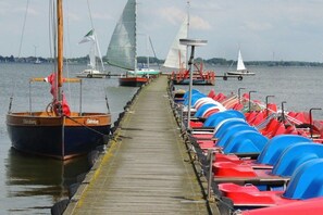 A wooden pier leading to a dock with several boats and a row of colorful kayaks. - Holiday home with 1 bedroom (Neuenkirchen)