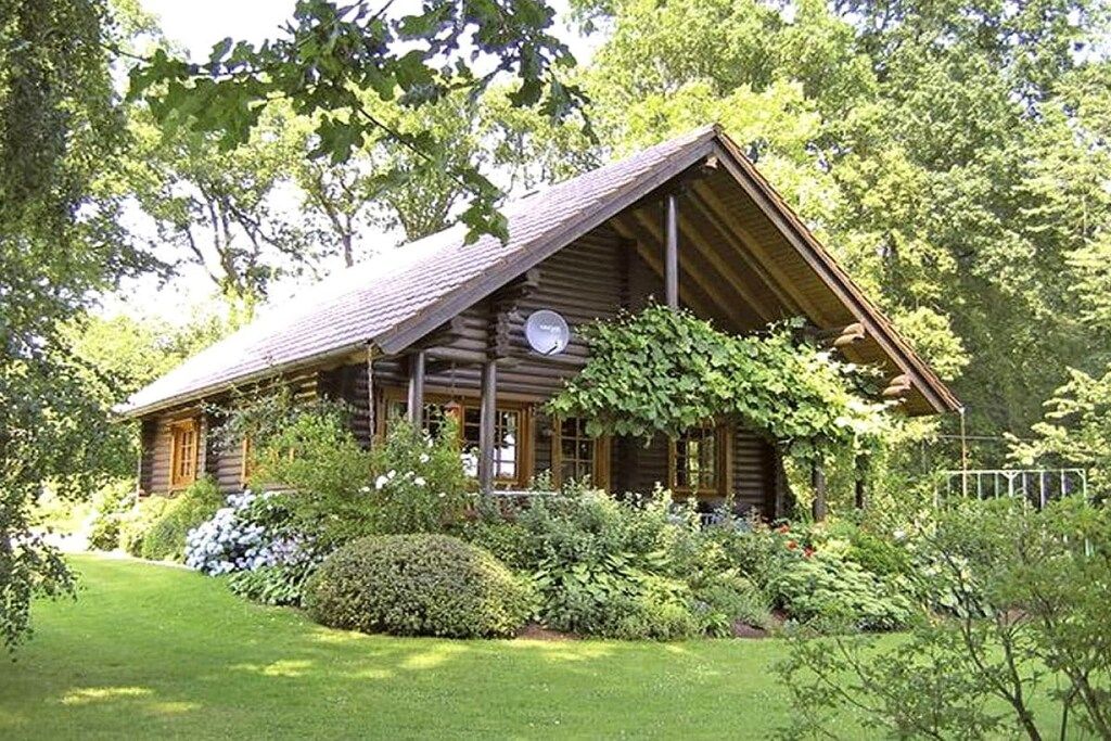 A wooden cabin with a sloped roof, surrounded by lush greenery and a well-maintained lawn.