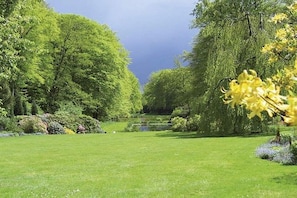 A well-maintained garden with a variety of trees and shrubs, a clear sky, and a small pond. - Holiday home with 1 bedroom (Neuenkirchen)