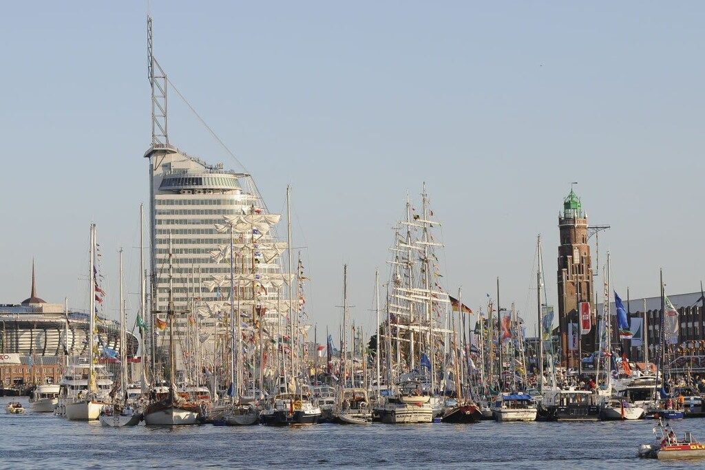 A marina with multiple sailboats docked, a prominent modern building, and a historic tower.
