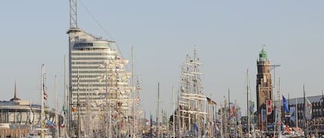 A marina with multiple sailboats docked, a prominent modern building, and a historic tower.