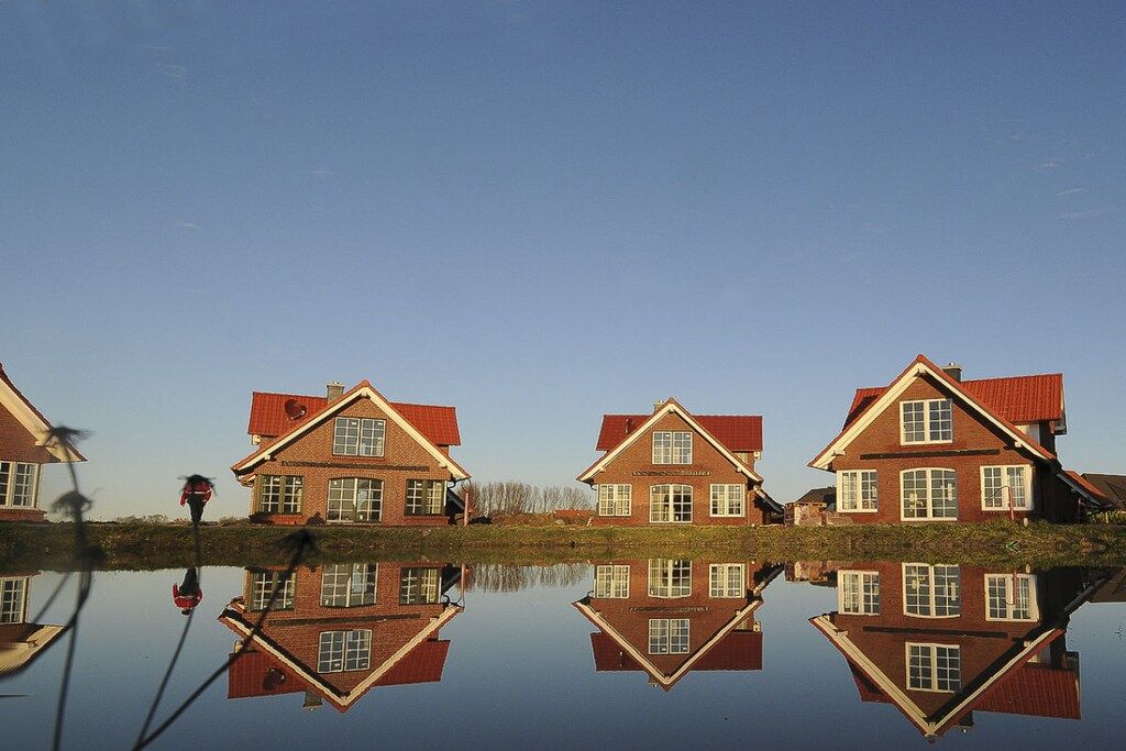 Et symmetrisk spejlbillede af en række huse med røde tage i stille vand.