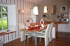 A dining area with a wooden table, white chairs, and a view of a garden through a window. - Pond View - Gundies Home No. 15 Ltd (Klein Meckelsen)