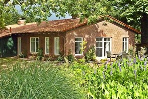 A brick house with a tiled roof, a front porch, and a garden with various plants. - Pond View - Gundies Home No. 15 Ltd (Klein Meckelsen)