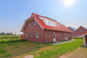 Une maison à deux étages, construite en briques et coiffée d’un toit rouge, avec un porche à l’avant et une pelouse bien entretenue.