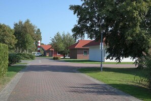 A paved pathway leading to a building with a red roof, surrounded by greenery and trees. - Holiday home in Butjadingen with parking (Butjadingen)