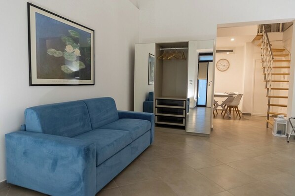 A living room with a blue sofa, a framed picture on the wall, and an open closet with a coat rack. - TREVISANI 221 APARTMENTS (Bari)
