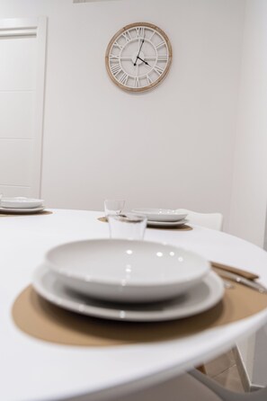 A dining table with plates and cutlery, a clock on the wall, and a door in the background. - TREVISANI 221 APARTMENTS (Bari)