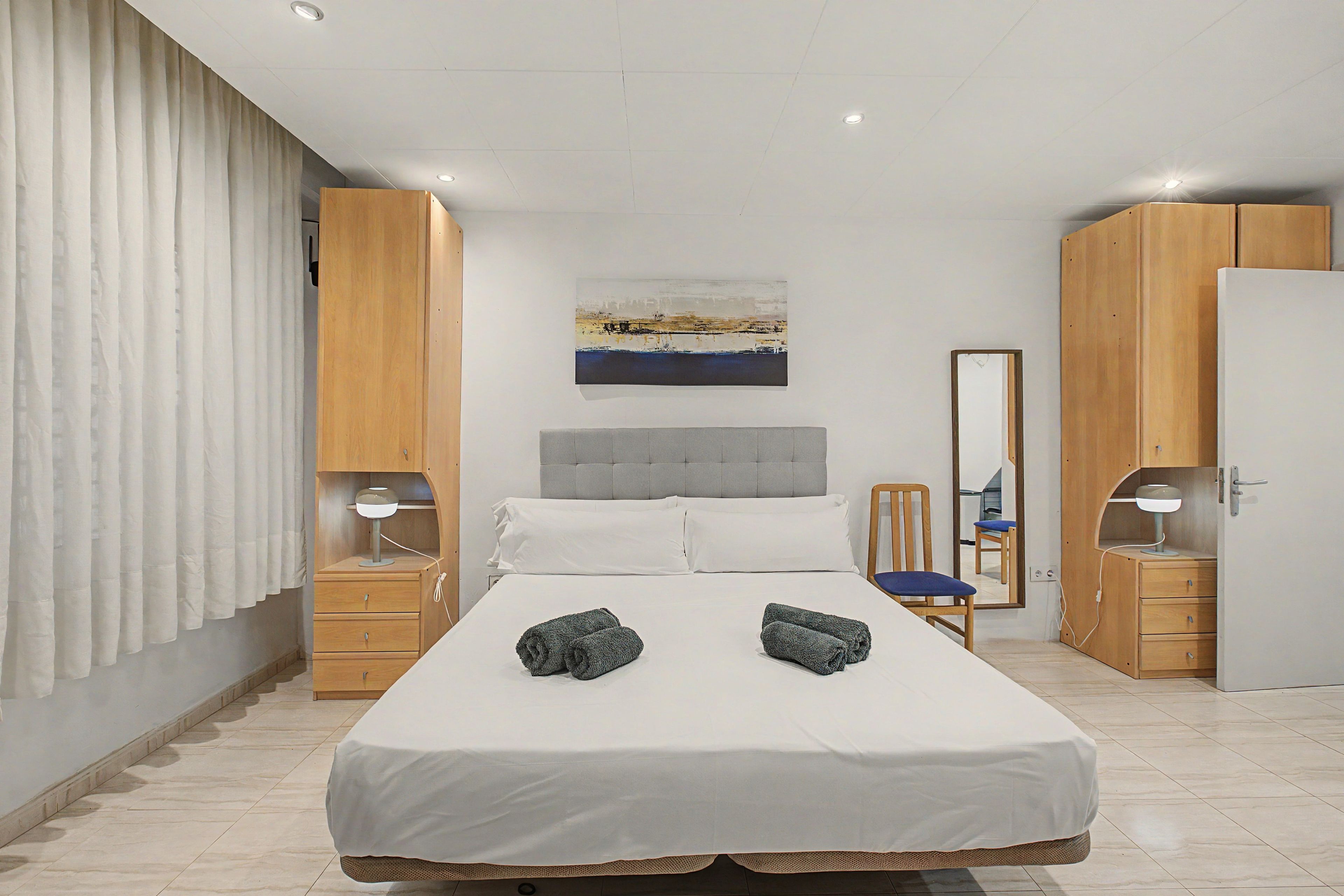 A modern bedroom with a large bed, a headboard, a bedside table with a lamp, a wardrobe, and a mirror.