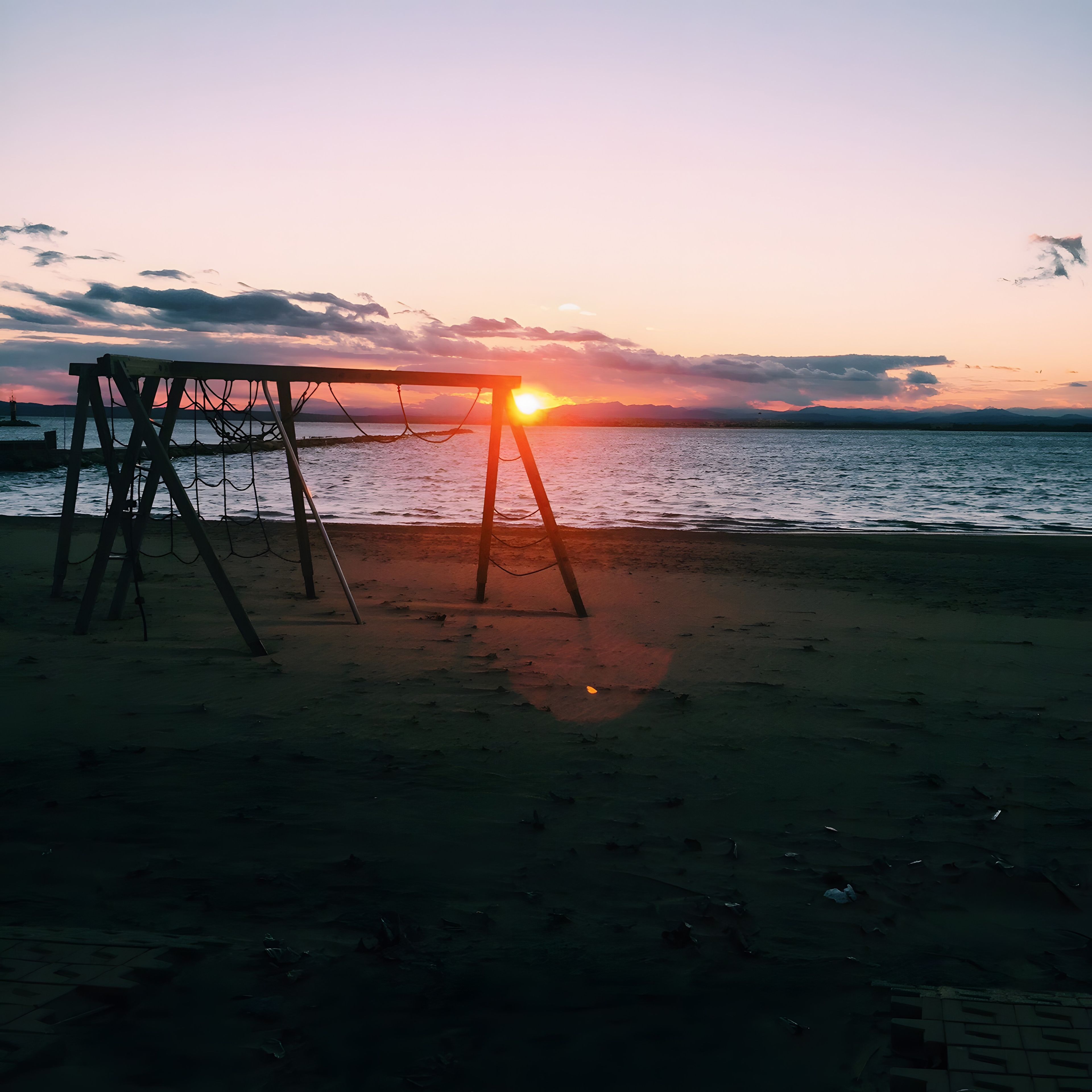Een strand met een schommel en een ondergaande zon.
