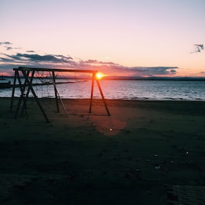 Een strand met een schommel en een ondergaande zon.