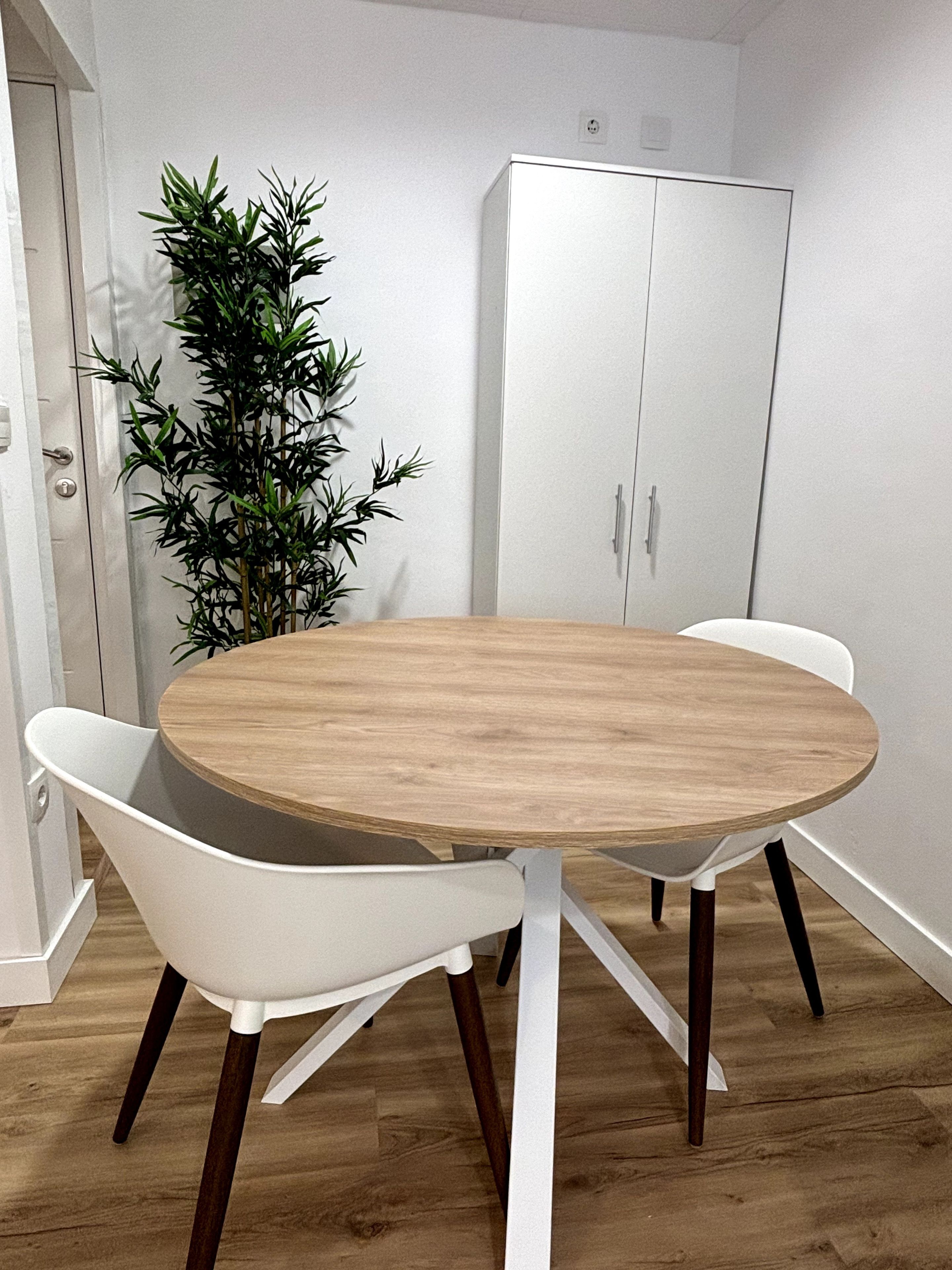 Een eethoek met een ronde houten tafel, witte stoelen en een wit kastje op de achtergrond.