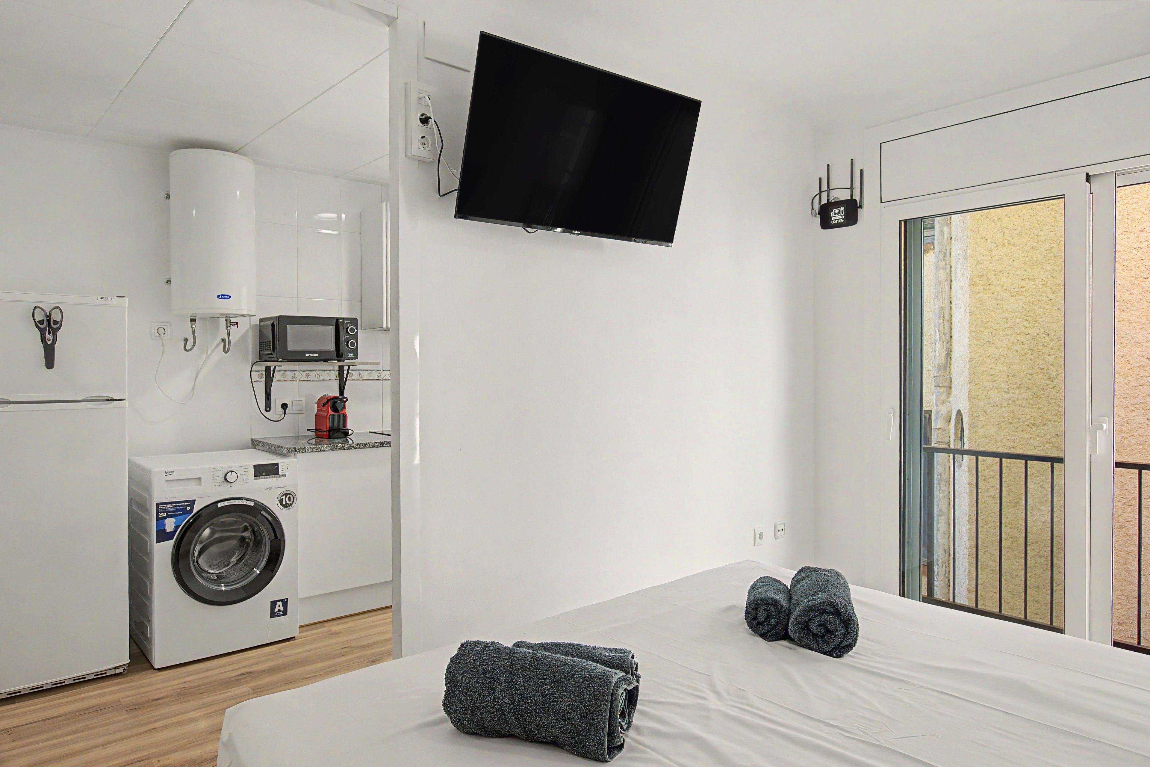 Une chambre d’hôtel équipée d’un lit, d’une machine à laver, d’un four à micro-ondes et d’un téléviseur fixé au mur.