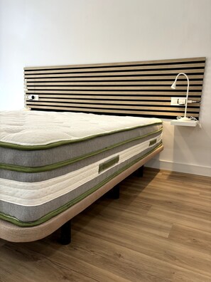 Een bed met hoofdbord, een bedlampje en een stopcontact.