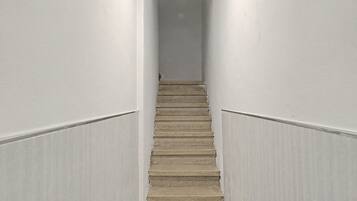 En smal trappa med mattbeklädd trappsteg, vita väggar och en svart och gul varningsrand högst upp.
