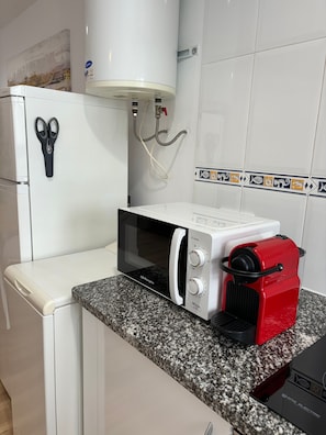 Een keuken met een magnetron, een rood en zwart apparaat, en een witte koelkast.