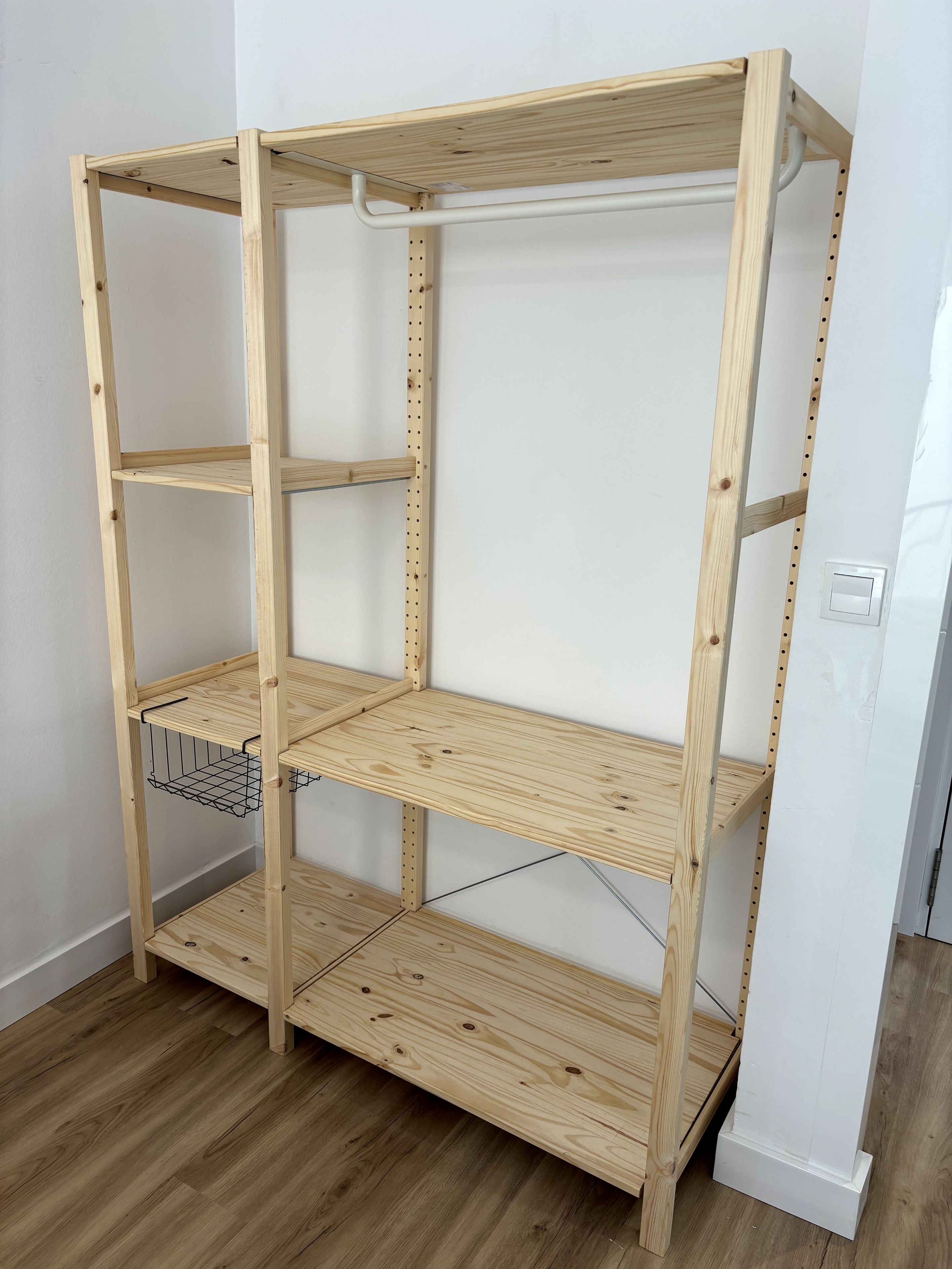 Een houten schapkas met verschillende planken, metalen draadmanden en een witte achtergrond.