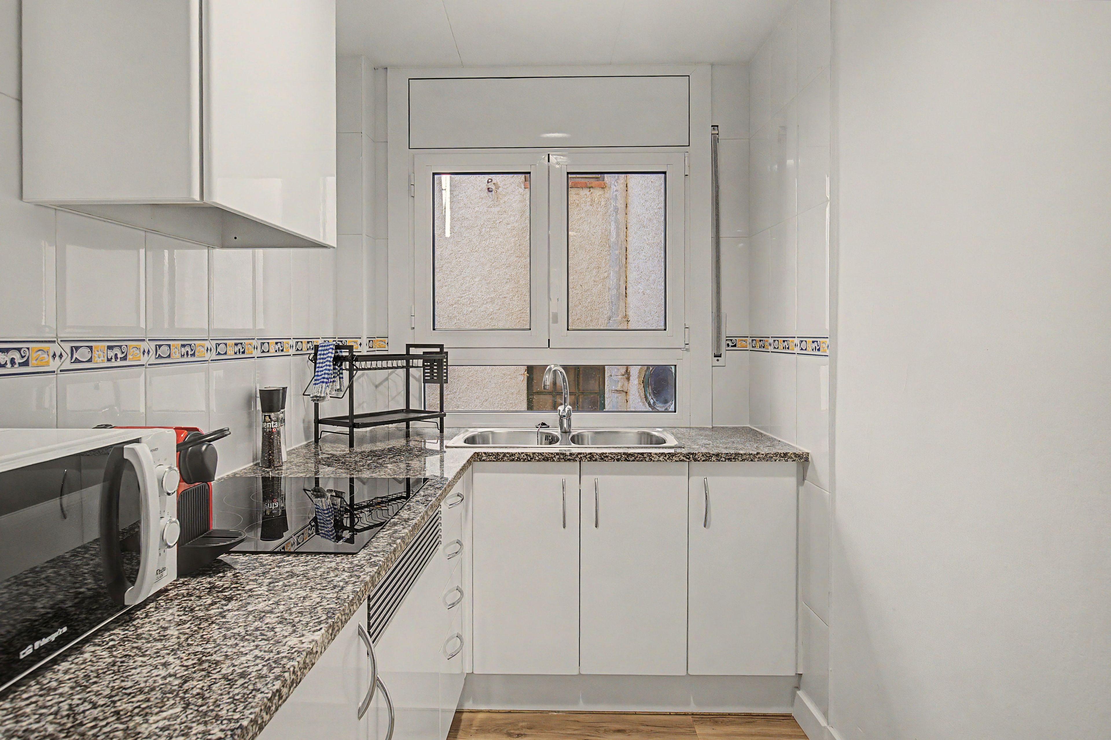 A compact kitchen with white cabinets, a granite countertop, a built-in oven, and a window above the sink.