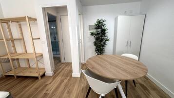 A room with a round wooden table, white chairs, a plant, and a wardrobe.