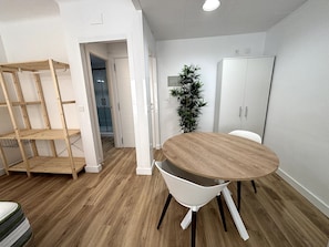 Een kamer met een ronde houten tafel, witte stoelen, een plant en een garderobe.