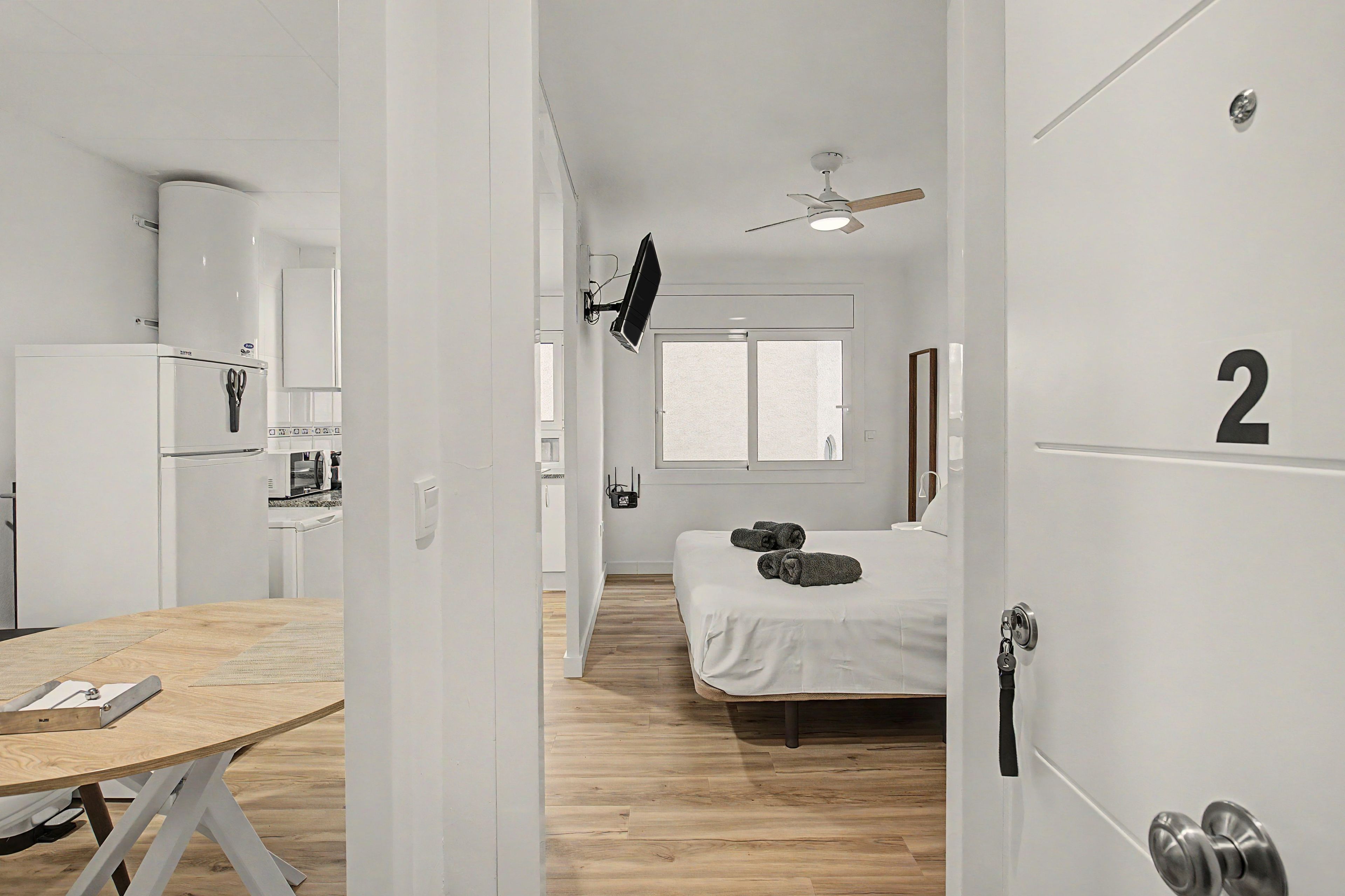 A modern, minimalist room with a bed, a small table, and a kitchenette.