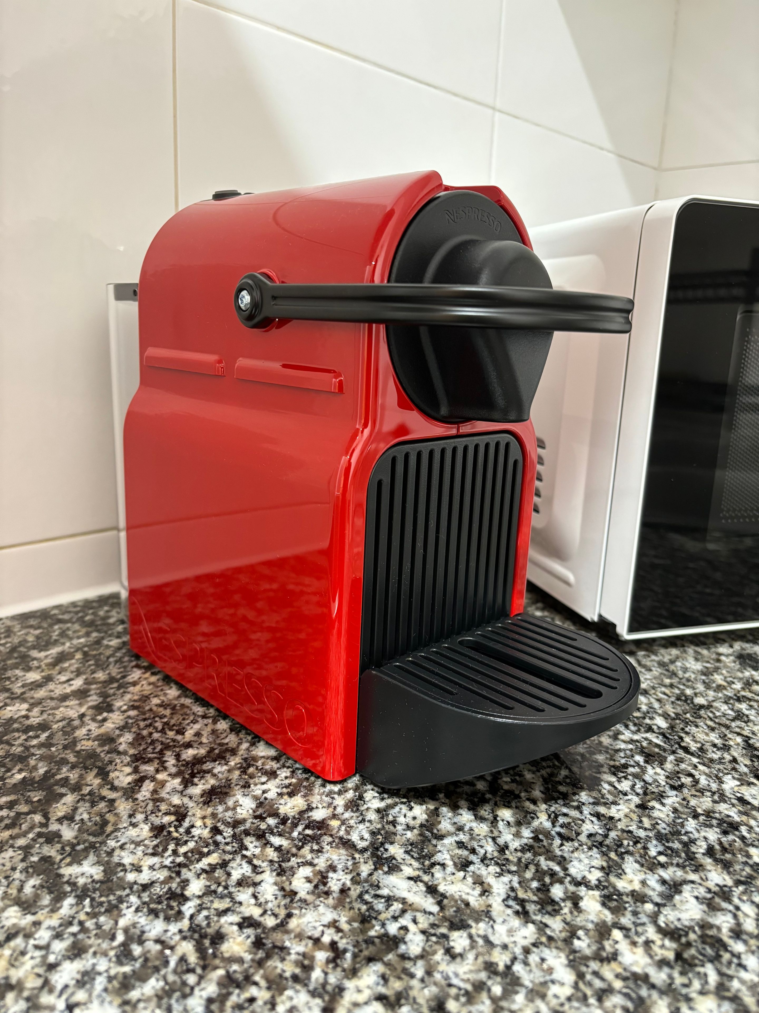 A red espresso machine with a black drip tray on a granite countertop.