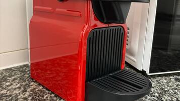 A red espresso machine with a black drip tray on a granite countertop.