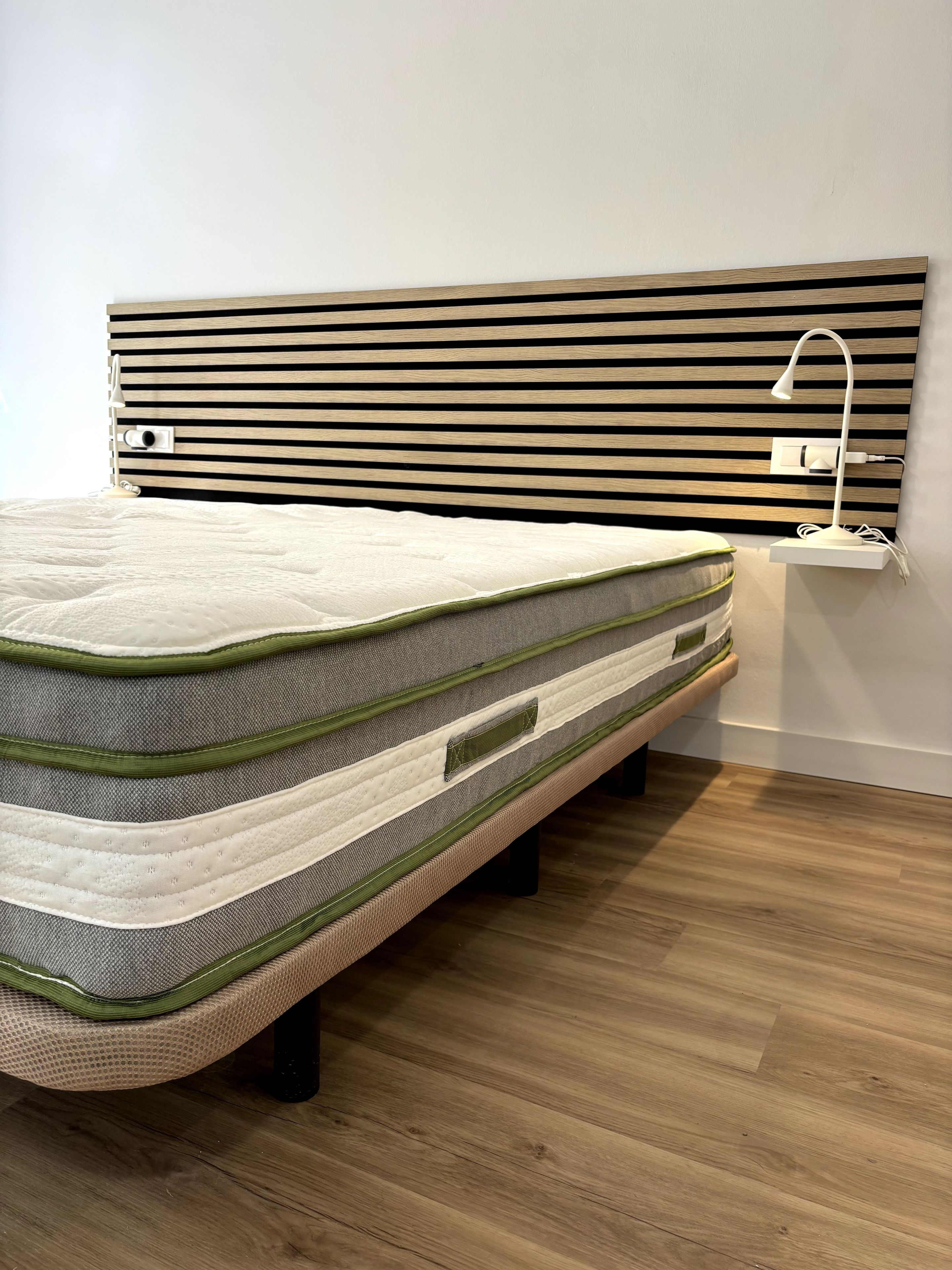 A bed with a headboard, a bedside lamp, and a power outlet on the wall.