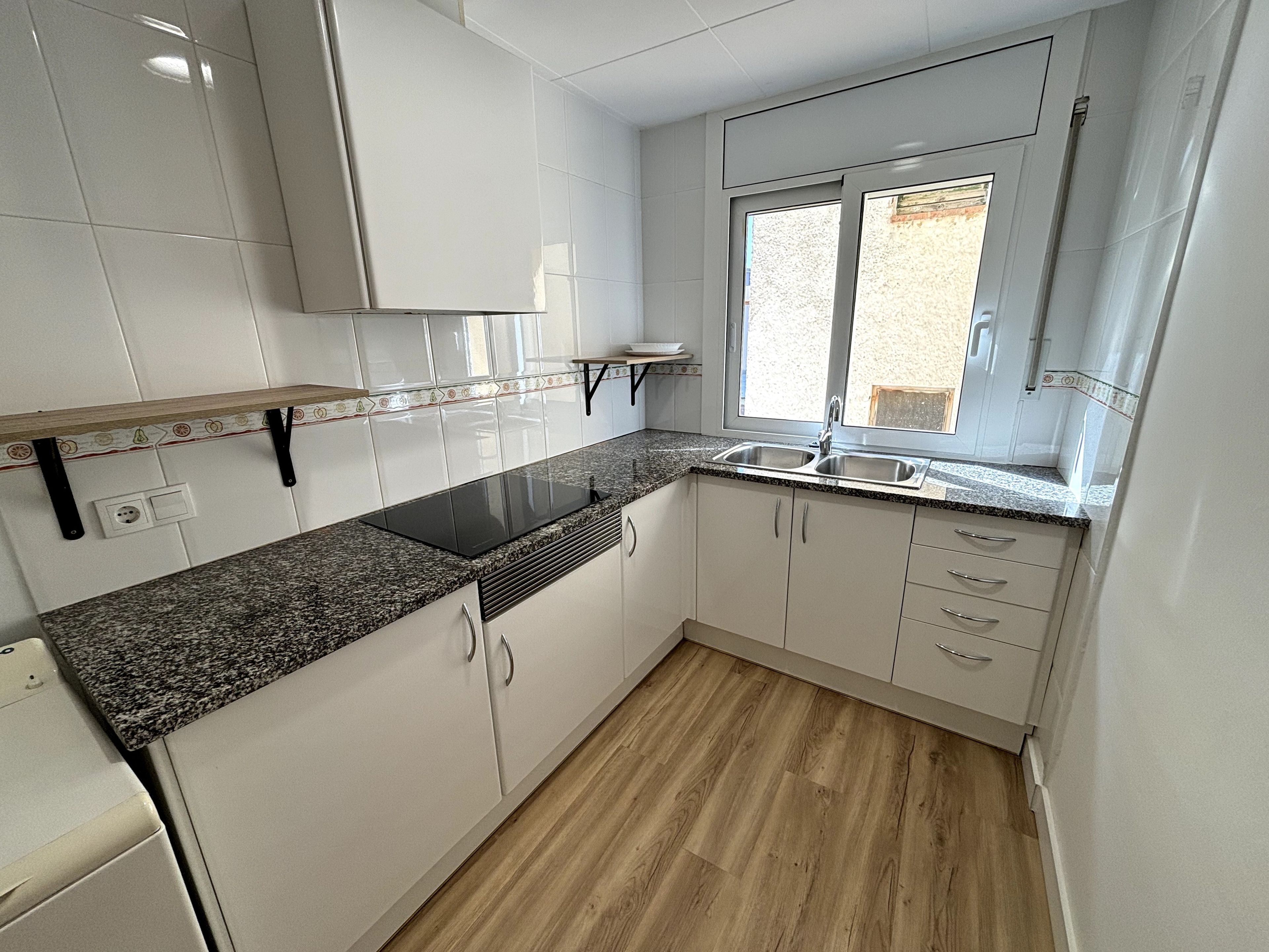 Une cuisine avec des meubles blancs, un plan de travail en granit, une plaque de cuisson à induction noire et une fenêtre donnant sur l’extérieur.