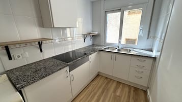 Une cuisine avec des meubles blancs, un plan de travail en granit, une plaque de cuisson à induction noire et une fenêtre donnant sur l’extérieur.