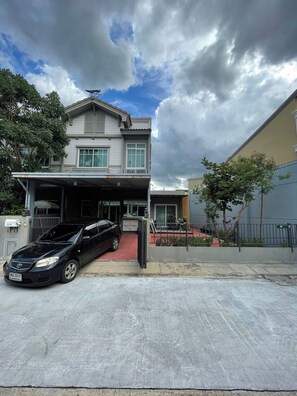 A two-story residential building with a covered garage and a black car parked in front. - Serene 2-bedroom House Rental in Bang Kaeo, Thailand (Bang Phli)