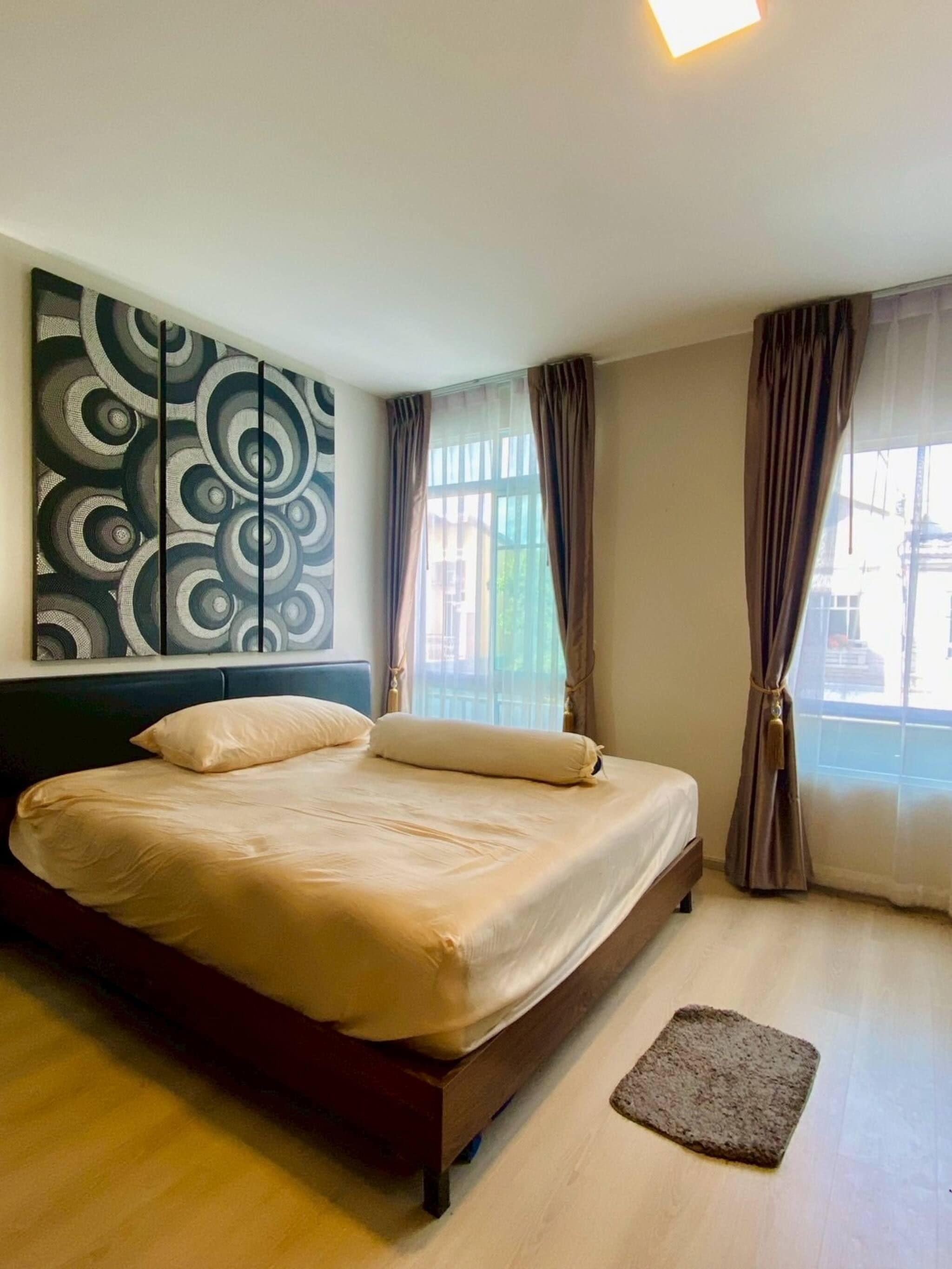 A bedroom with a bed, a headboard, a wall with a circular pattern, and a window with curtains.