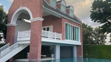 A house with a swimming pool, a brick facade, and a balcony.