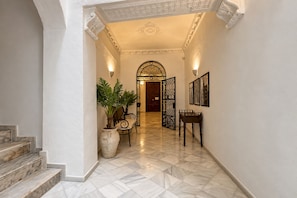 A marble-floored hallway with a staircase, a potted plant, a chair, a table, and a door with an ornate archway. - Genteel Home Patio del Arenal 001 (Seville)
